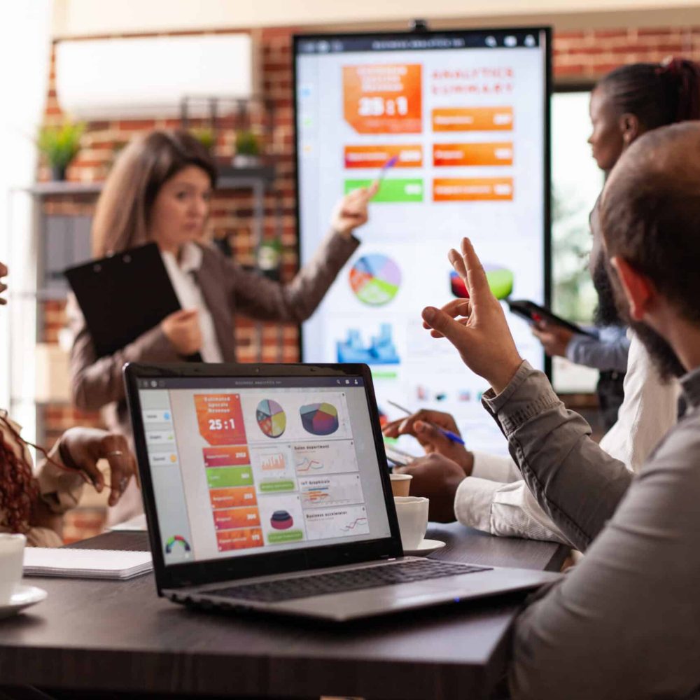 Executive manager explaining marketing strategy showing company graph on monitor discussing business collaboration with businessteam. Diverse entrepreneurs working at project in startup office